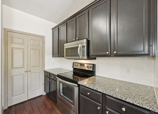 A kitchen with dark brown cabinets and a granite countertop.