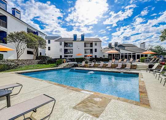 a swimming pool with lounge chairs and umbrellas in front of a building