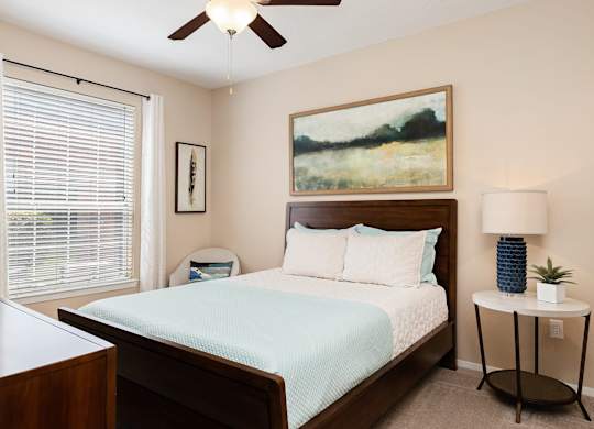 A bedroom with a bed, nightstand, and a painting on the wall.
