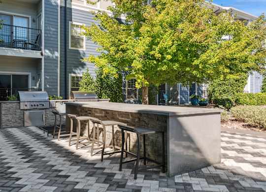A patio with a bar and chairs is surrounded by a building and trees.