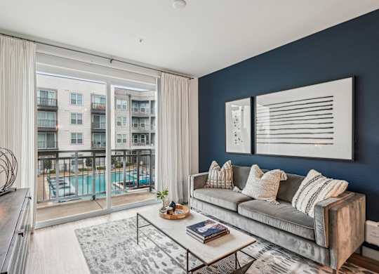 A modern living room with a grey sofa and a large window overlooking a pool.