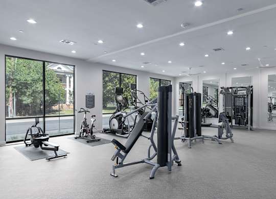 A spacious gym with a variety of equipment and a view of trees outside the windows.