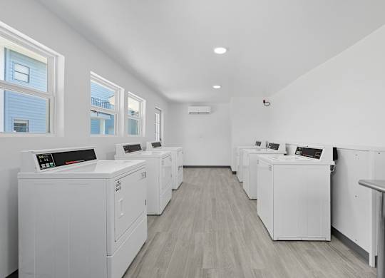 A row of white washing machines are lined up in a laundry room.