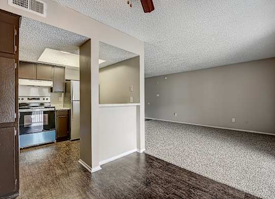 an empty living room with a kitchen in the background