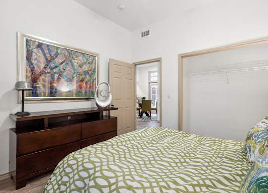 A bedroom with a bed, a dresser, and a painting on the wall.