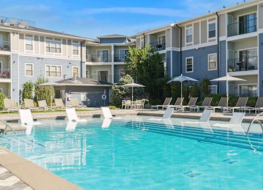 A swimming pool with lounge chairs and umbrellas in front of apartment buildings.
