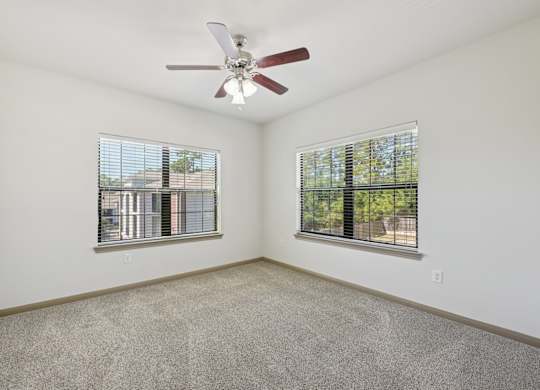A room with a ceiling fan and two windows.