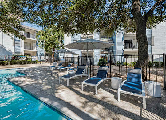 A pool surrounded by chairs and trees.