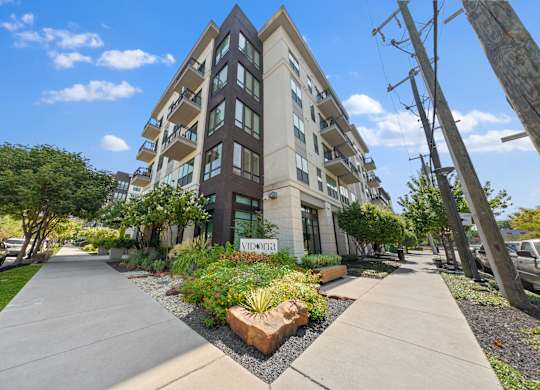 A modern apartment building with a landscaped courtyard in front.