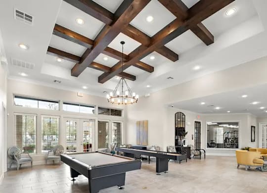 A large billiard table is in the middle of a spacious room with a high ceiling and wooden beams.