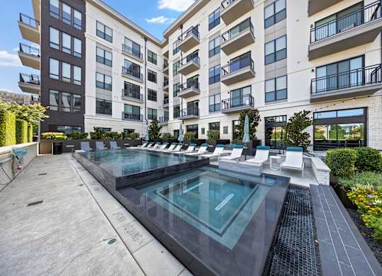 A large outdoor pool surrounded by lounge chairs and buildings.