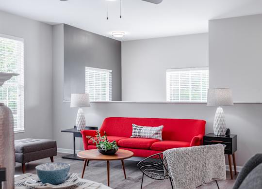 A living room with a red couch and a table with a plant on it.
