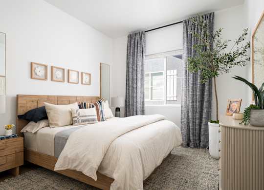 A bedroom with a large bed, a nightstand, a dresser, and a window with curtains.
