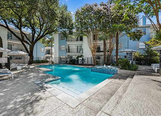 A pool surrounded by trees and apartment buildings.