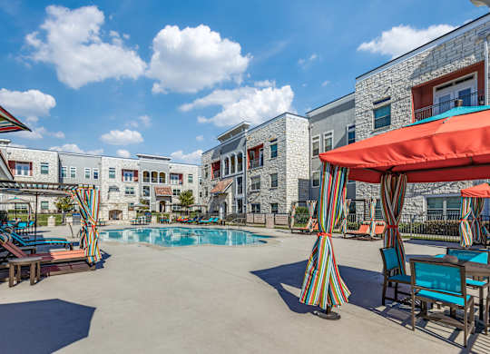 A pool area with a striped umbrella and chairs.