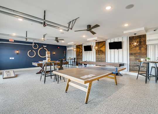 A ping pong table is in the middle of a room with a blue wall and a ceiling fan.