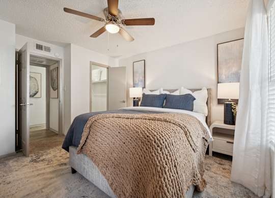 A bedroom with a bed covered in a brown blanket and a ceiling fan.