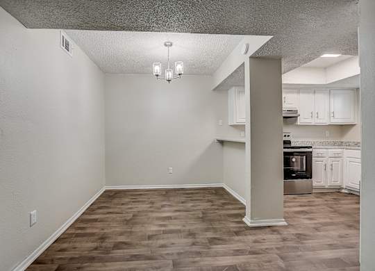 an empty living room with a kitchen in the background