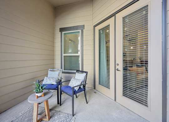 Private patio with beige siding featuring glass-framed French doors and a sliding casement window, furnished with an outdoor seating set.