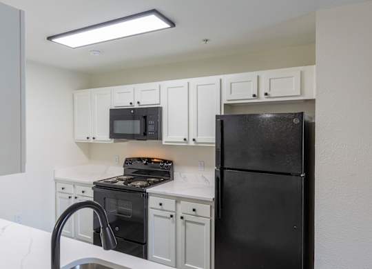 A black refrigerator sits in a kitchen with white cabinets and a black stove.