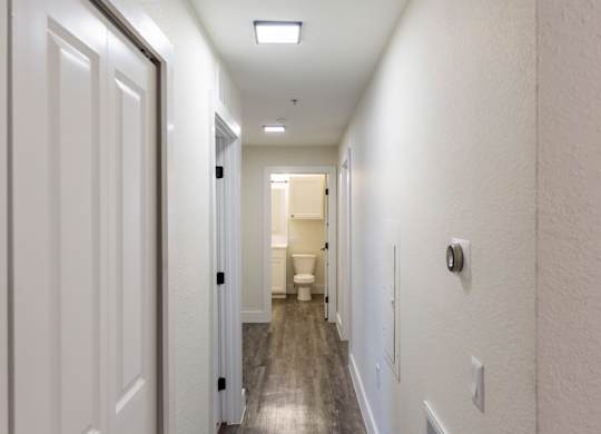 A long white hallway with doors on both sides and a light on the ceiling.