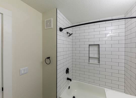 A white tiled shower with a white tub and a black shower head.