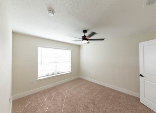 A room with a ceiling fan and a window with blinds.