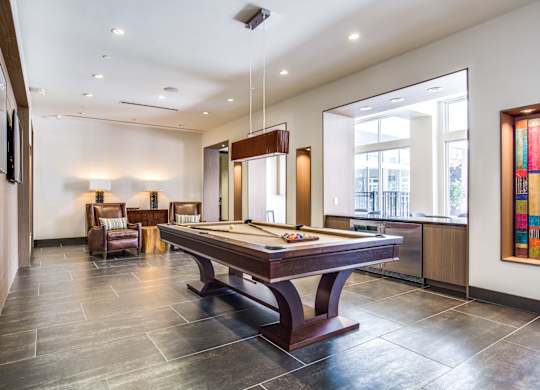 A room with a pool table and chairs.