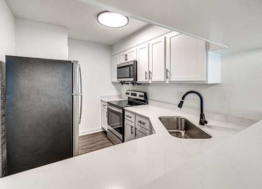A kitchen with a black refrigerator, white countertops, and stainless steel appliances.