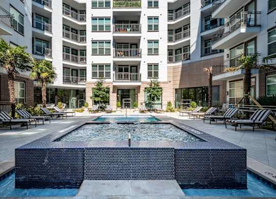 A large pool in the middle of a courtyard surrounded by lounge chairs and palm trees.