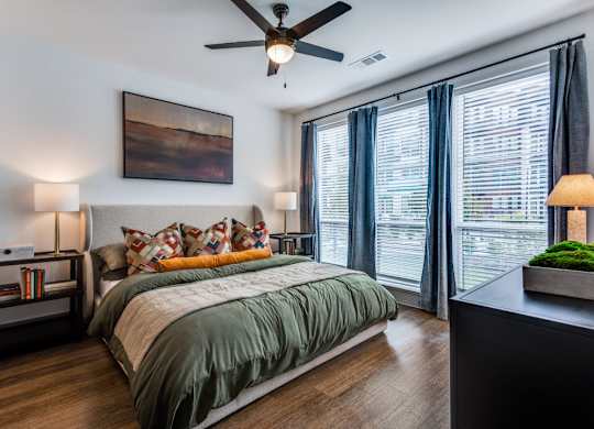 A bedroom with a bed, a ceiling fan, and a painting on the wall.