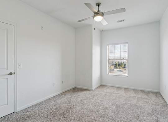 A room with a ceiling fan and a window with blinds.