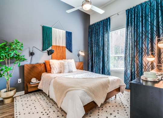 A bedroom with a bed, a potted plant, and a ceiling fan.