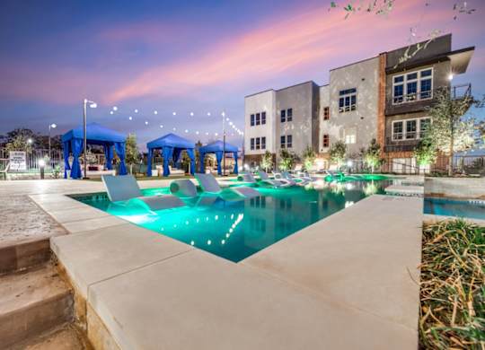 A swimming pool area with a building in the background at dusk.