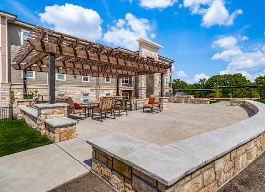 a patio with a stone wall and a wooden pergola