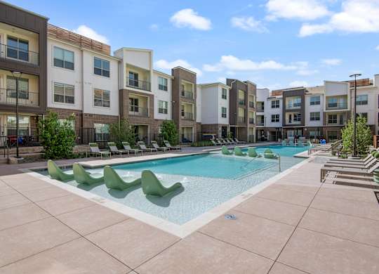 A swimming pool surrounded by lounge chairs in front of apartment buildings.