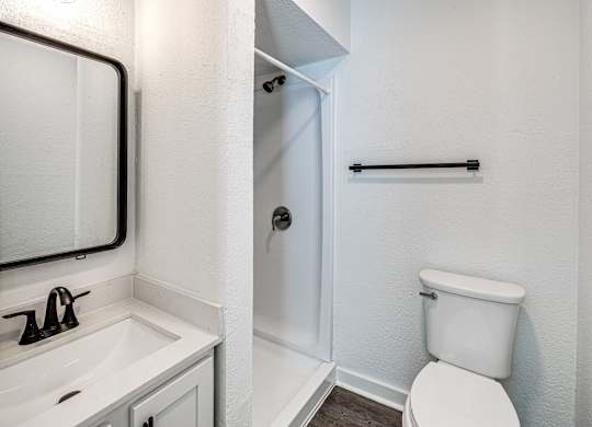 A white toilet in a small bathroom with a white sink and a mirror.