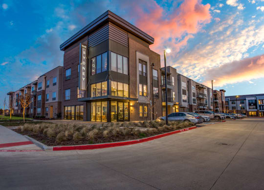 an apartment building at dusk with the sun setting behind it