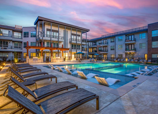 an apartment pool with lounge chairs at dusk
