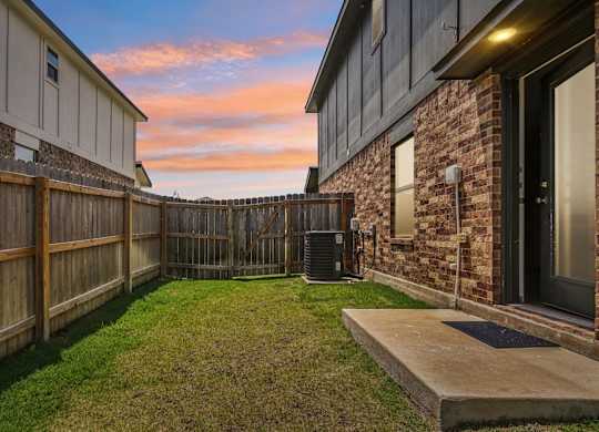 A backyard with a wooden fence and a brick house.