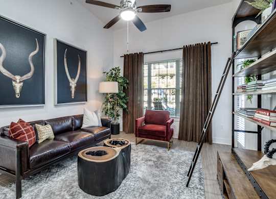 A living room with a black couch, a red chair, and two bull skulls on the wall.