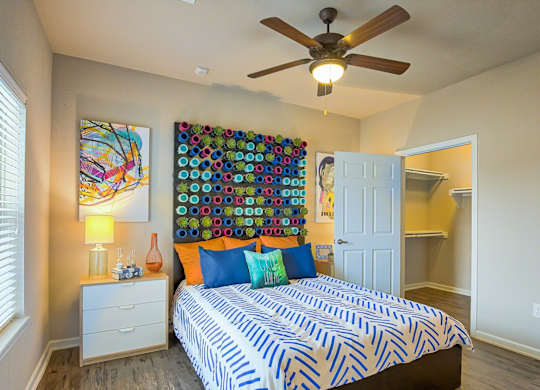 A bedroom with a bed, a ceiling fan, and a wall hanging.