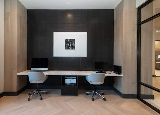 A black and white photo is on the wall above a desk with two chairs and a computer.
