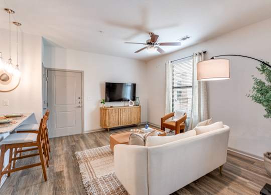 A living room with a white couch, a wooden dining table, a television, and a ceiling fan.