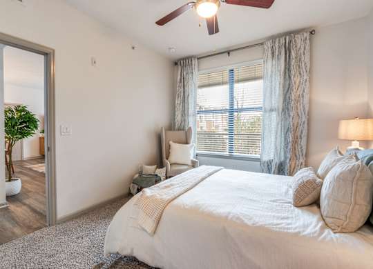 A bedroom with a large bed, a ceiling fan, and a window with blinds.