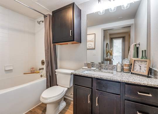A bathroom with a white toilet, a bathtub with a shower curtain, and a mirror above the sink.