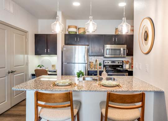 A kitchen with a granite countertop and wooden chairs.