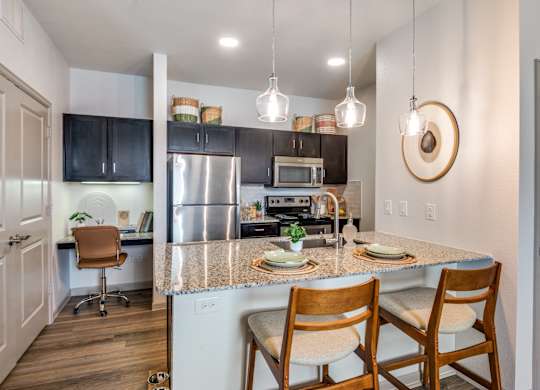 A kitchen with a table and chairs in the foreground and a refrigerator, microwave, and oven in the background.