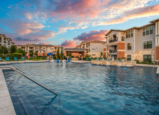 a swimming pool with buildings and a sunset in the background