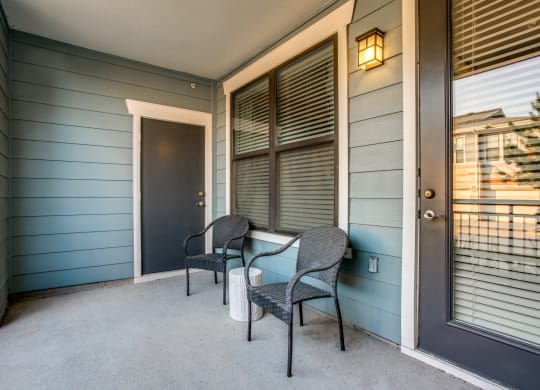 the front porch of a house with two chairs and a door